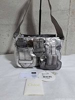 Front view of metallic silver Chloé Saskia bag with booklet, authenticity card and swing tag visible