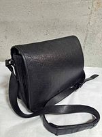 Front view of black Guccissima leather messenger with flap closed and strap visible