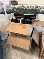 Toshiba VCR on stack of VHS tapes in open box showing quantity