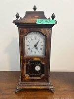 Front view of mantel clock showing dial, pendulum window, case finish, metal feet