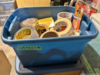 Top view of blue bin containing assorted tape rolls and Gorilla mounting squares package