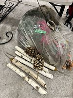 Bagged assortment of artificial flowers, birch stakes and pinecone picks on floor