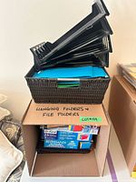 Stacked black plastic trays on wicker basket over box of folders