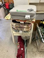Stack of seat cushions on two plastic chairs, green/white rolled umbrella and red folding chair bag on floor