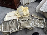 Three beige zippered storage bins with clear windows plus folded cream hanging shelf units on floor