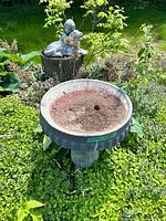 Bird bath basin on pedestal in garden with statue visible behind