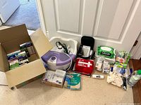 Lot overview showing boxed bandages, foot spa, first aid kit, blood pressure monitor and other supplies