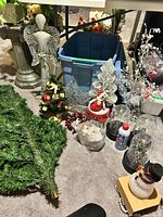 Overview of lot showing angel statue, storage tote, LED twig sprays, ornaments, tins and snowman