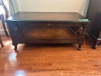 Front view of cedar chest showing carved rosettes, bracket feet, veneer finish