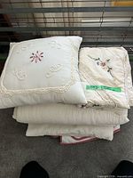 Stacked decorative pillow, folded embroidered quilt and sham, additional quilts underneath