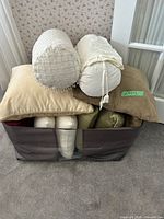 Pillows stacked in brown fabric bin, showing beige square pillow and two ivory bolsters on top