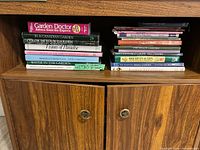 Two stacks of assorted gardening books inside cabinet