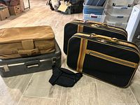 Overall view showing tan suitcase atop gray hard case, two black striped suitcases and waist pack