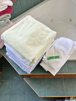 Stack of assorted color cotton terry towels on bathtub edge