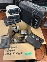 Overall lot showing stack of clock radios, Superadio, travel radios, CD players and earbuds in box