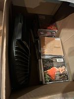 Open box showing black plastic tray and stacked jewel-case CDs