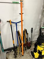 Group shot of assorted long-handle garden tools leaning against wall