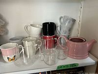 Shelf view showing assorted ceramic mugs, clear double-wall glass mugs, and pink teapot