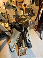 Overall view of tan bag on pull cart, white carry bag, clubs, and wooden racket