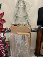 Two boxed and bubble-wrapped metal frame lighted Christmas trees visible