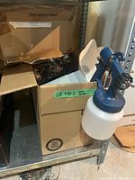 Blue spray gun with white paint cup and open box