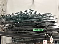 Stack of bundled green and black metal folding fence panels on shelf, tags visible