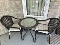 Overall view of two wicker chairs, round glass-top table and cushions