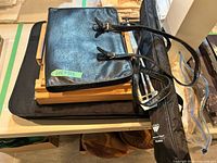 Stacked view showing black leather-like carrier on top of wooden pochade box, nylon tripod bag underneath
