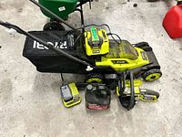 Lawn mower with grass bag, chargers, battery, chainsaw, oil container visible