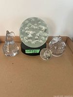group shot of four blown glass paperweights on cardboard surface