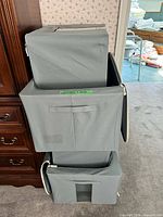 Three stacked gray fabric storage bins showing handles, clear windows and zippered tops