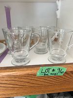 Six matching clear glass footed mugs on shelf