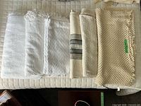 Six folded throw blankets in neutral colours showing patterns and fringe