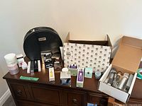 Overview of entire lot on dresser showing cosmetic bag, boxed skincare, cardboard boxes