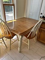 Dining table with two chairs, showing natural wood top and cream turned legs