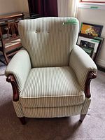 Front view of striped upholstered armchair showing button-tufted back, carved wood arms, removable cushion, front legs