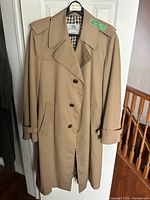 Full view of tan trench coat on hanger showing front buttons, collar, cuffs and pockets