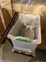 Plastic storage bin containing hoops, packaged kits and tools; brown wood poles leaning