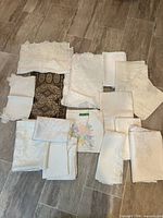 Group of assorted ivory, white and printed tabletop linens laid out on tile floor