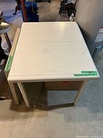 Top view of white laminate folding table showing surface scratches, edge chips and center leaf seam