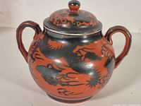 Front view of lidded sugar bowl showing red and black dragon design, twin handles