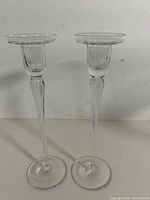 Full view of both clear glass candlesticks standing upright
