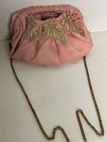 Front view of pink satin handbag showing appliqué detail and chain strap