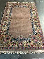 Full view of the handmade wool rug showing central field, floral border and fringe