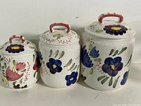 Front view of three hand-painted floral ceramic canisters with lids
