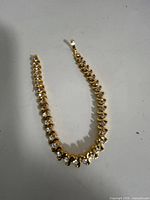 Full view of curved tennis necklace showing gold-tone setting and clasp