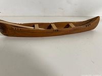 side view of carved wood canoe with paddle and thwarts visible