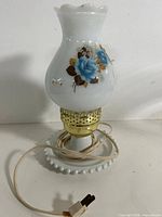 Full view of milk glass hurricane lamp with blue rose decal, cord coiled on base