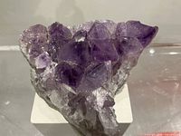 Front angled view of purple amethyst cluster on white stand