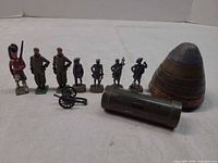 Group shot showing seven metal toy soldiers, small cannon, face-paint stick tube and conical fuze